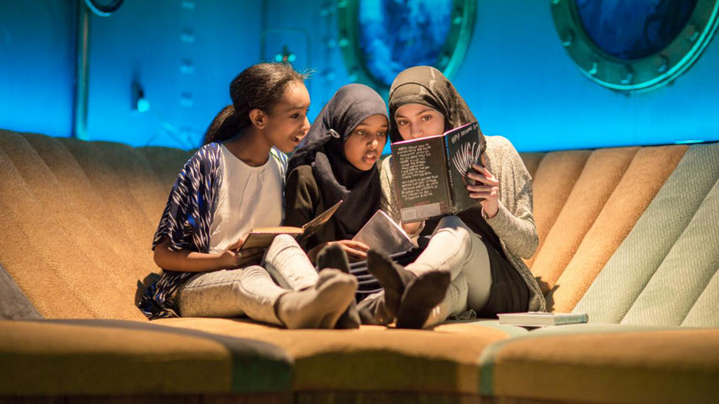 Tre barn sitter og leser bok på Tøyen Deichmanske bibliotek